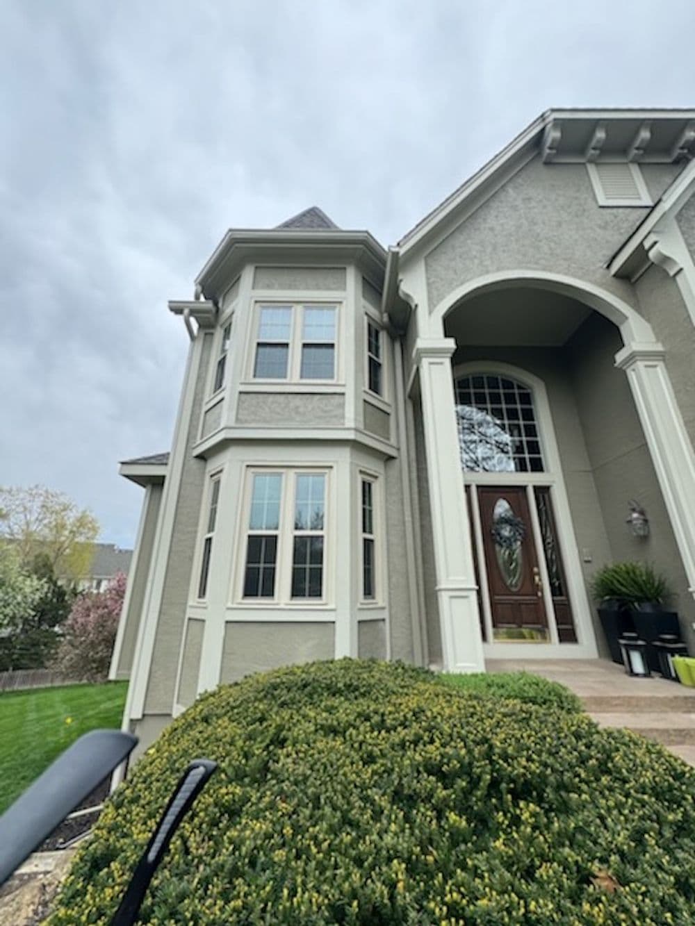 Elegant gray house with a tall entrance and bay window, surrounded by lush greenery.