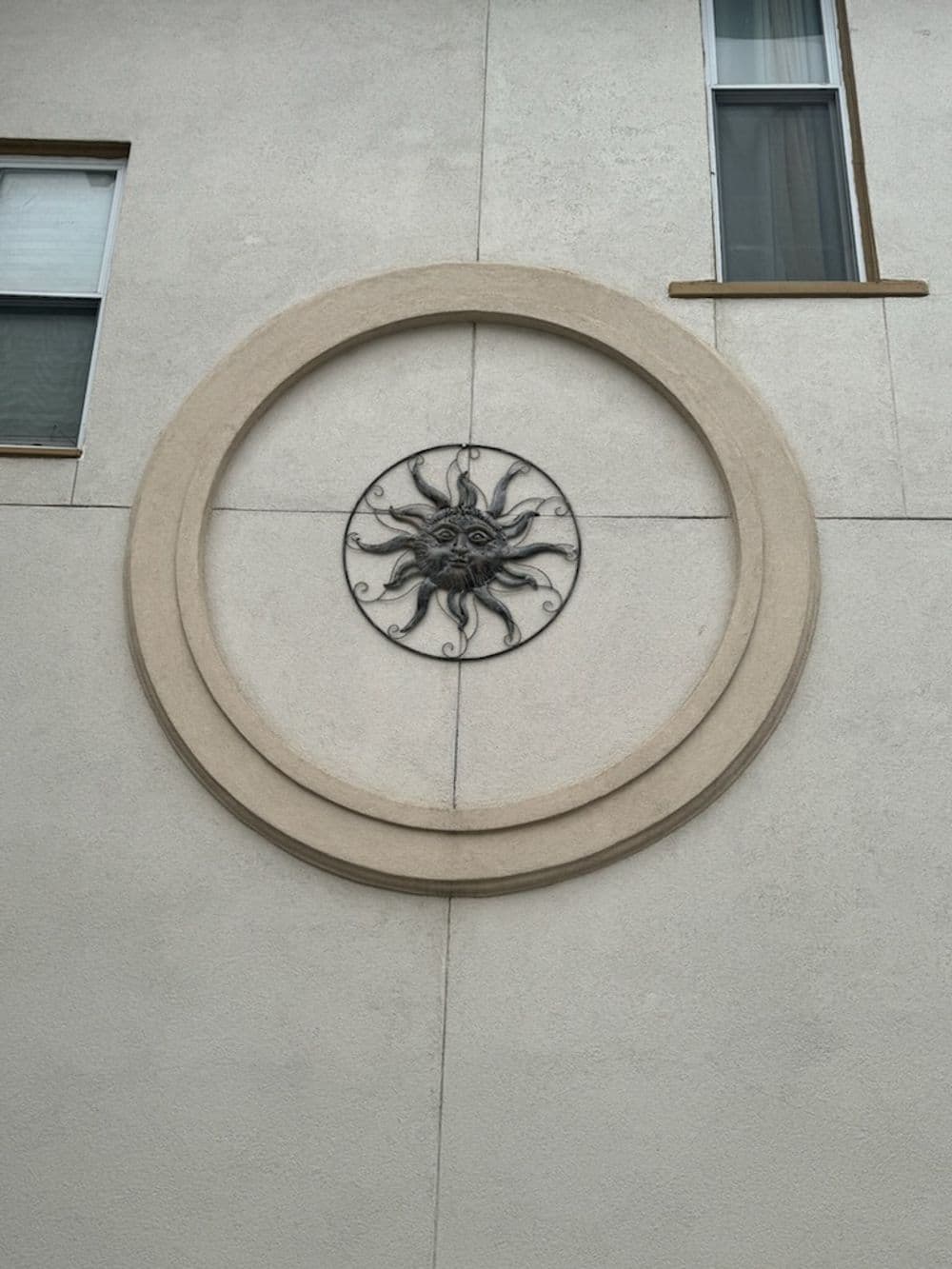 Sun motif sculpture set in a circular frame on a beige wall.